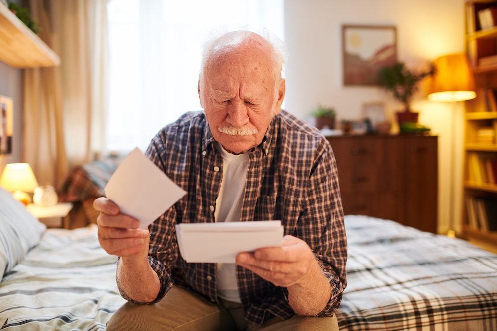 Old man sitting on the bed in bedroom and thinking about his health risk factors 