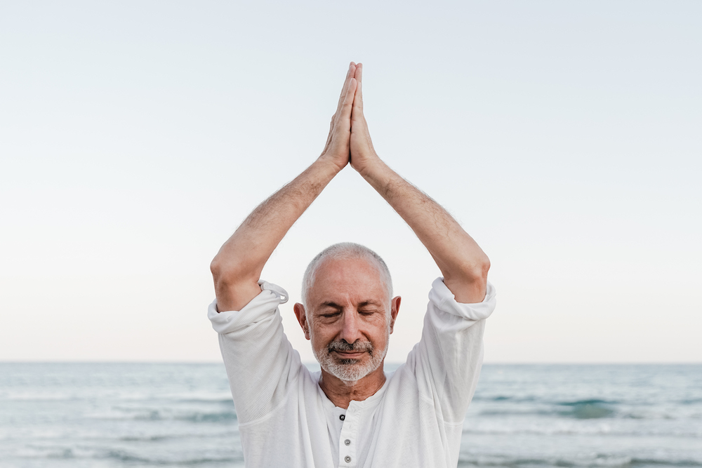 Senior man doing yoga meditation outdoor at the beach - Elderly and healthy lifestyle - Focus on face