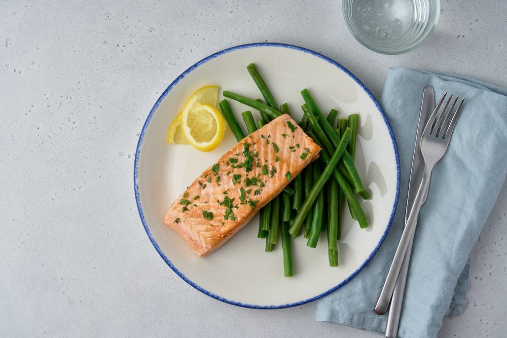 Tender baked salmon fillet in olive oil with parsley and lemon slice. Garnish boiled asparagus. Diet dish full of fats and omega 3. Healthy easy meal for pescetarians. Glass of water. meat free meal
low red meat diet 