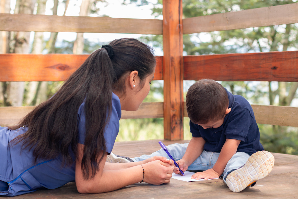 Latina pediatrician teaching writing and drawing to a child with a disability.