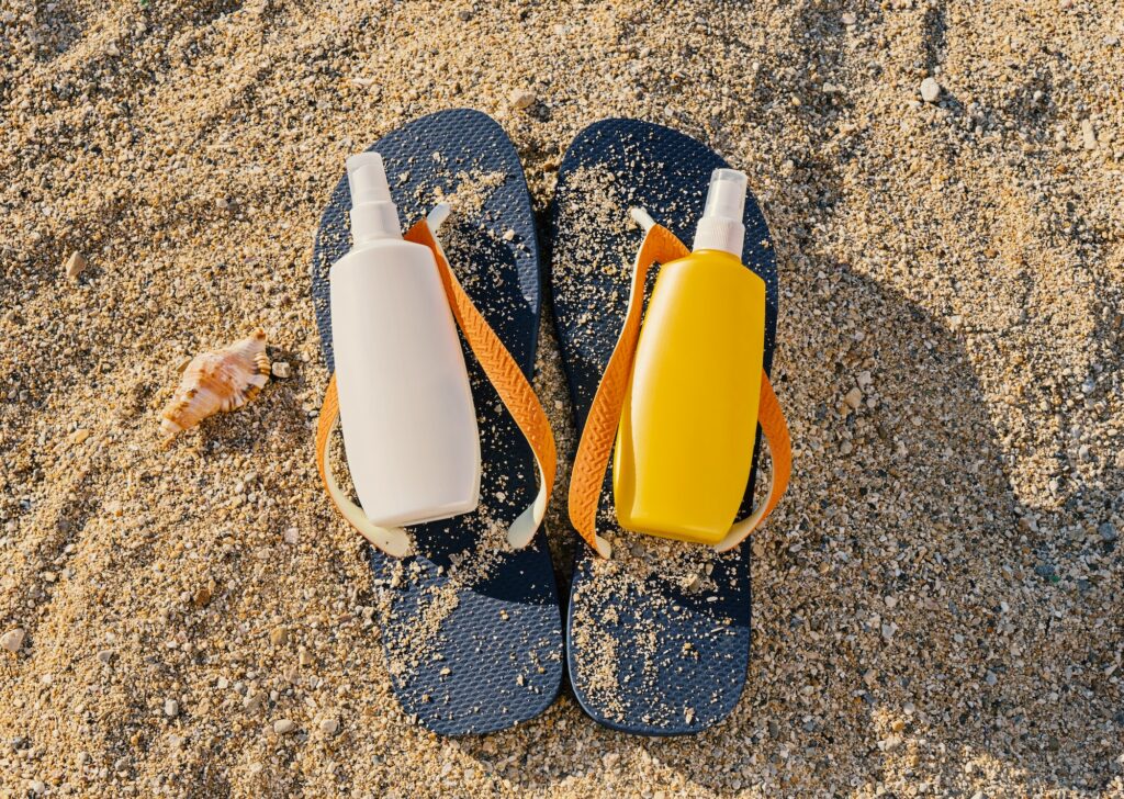 Top view of blue flip-flop and two bottles with sun protection spray. Summer skin care concept