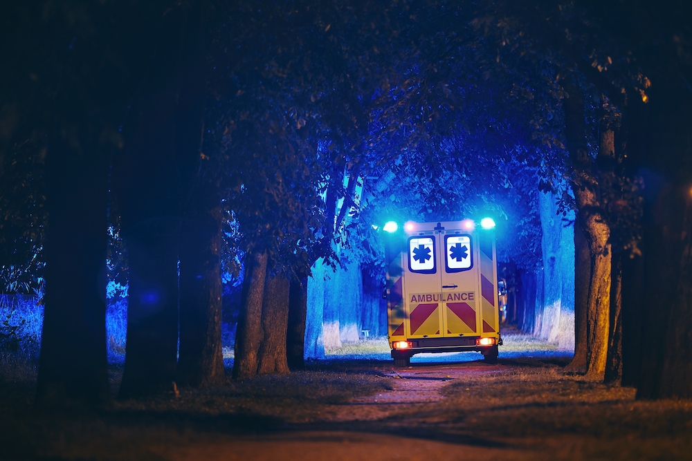 Rescue in dark alley. Rear view of ambulance of emergency medical service against illuminated trees from blue flasher. Ambulance cover in australia